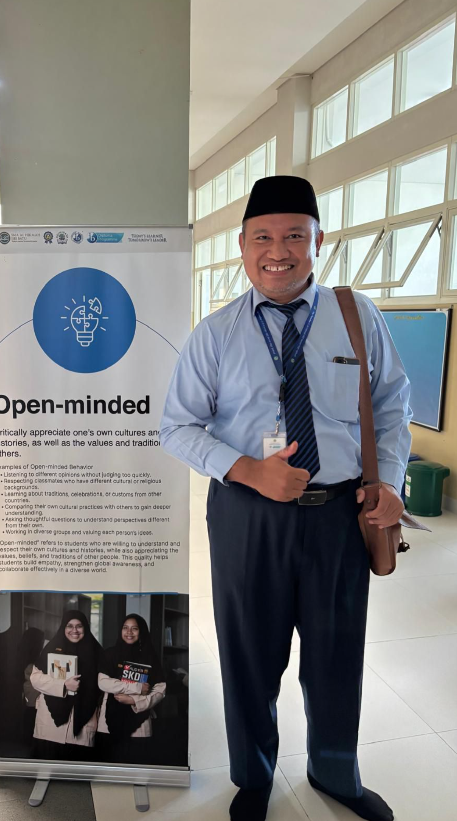 Pak Iwan from Al Hikmah school, standing next to one of the banners of IB Learner Profiles around the school